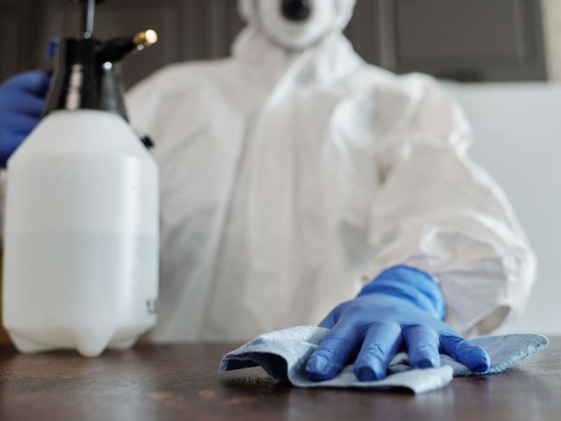 Gloved technician in protective suit disinfecting a work surface