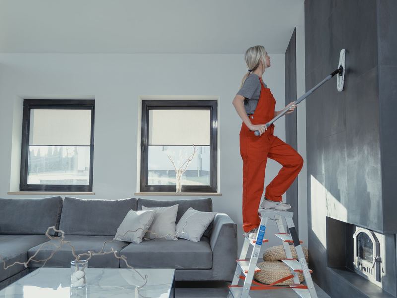 Cleaner on a step ladder cleaning walls in an empty, move-in-ready living room